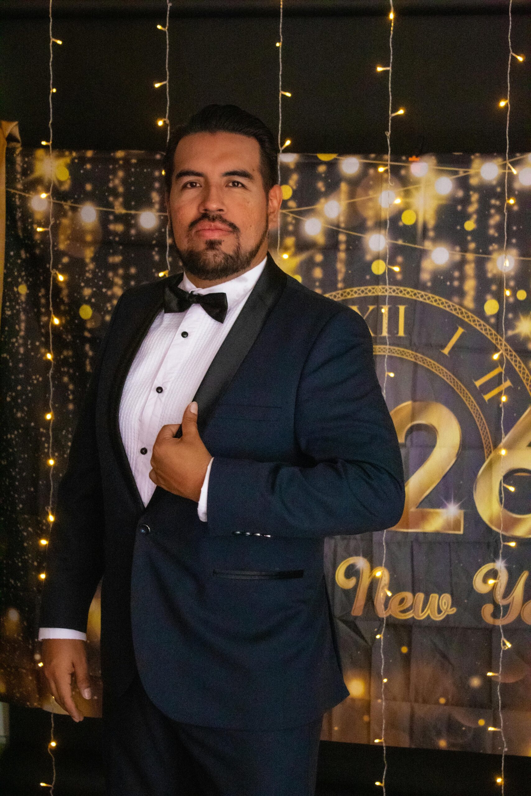 A man in a tuxedo celebrates New Year's Eve with festive decorations in a studio.